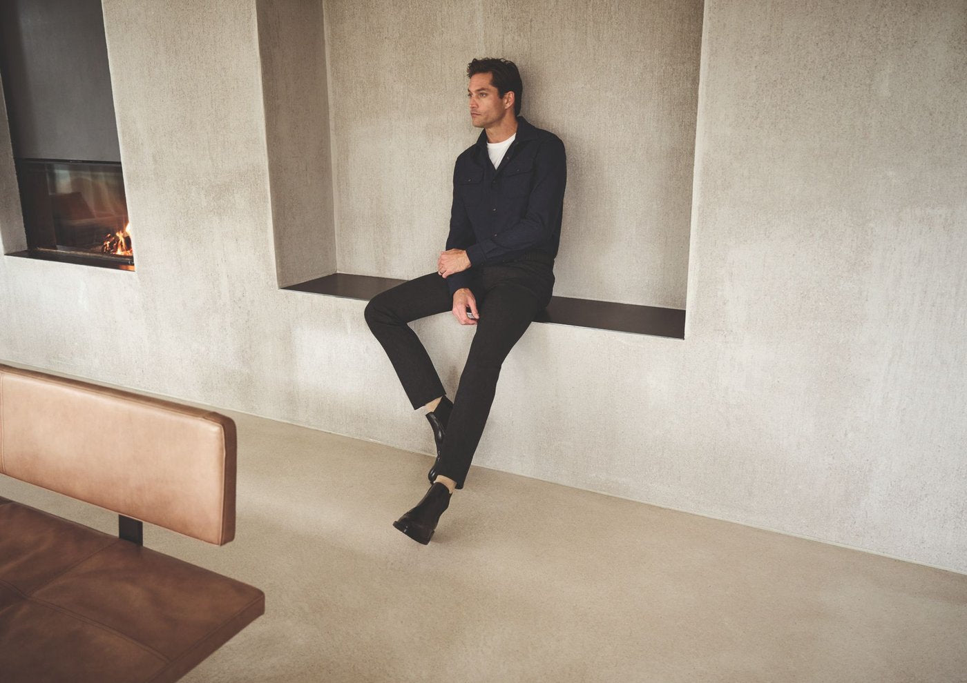 Alberto Pants — Man in navy overshirt and dark trousers seated in a concrete alcove